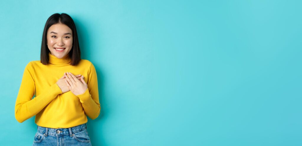 Woman against blue background with hands over her heart